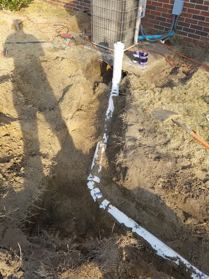 Trenched yard with white PVC pipe laid in dirt near a brick house and a shadow on the ground