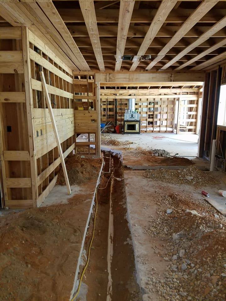 Interior of a house under construction with exposed wooden framing and a trench running through the floor