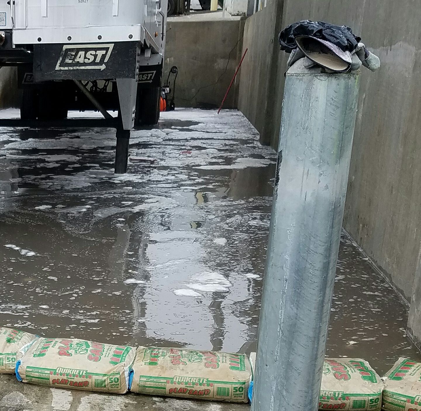 Flooded construction area with a truck, wet concrete, and stacked cement bags against a wall