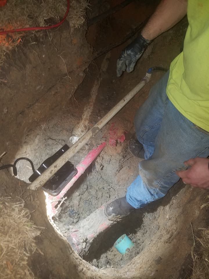 Person digging in a narrow trench with a shovel, wearing jeans and a yellow shirt.