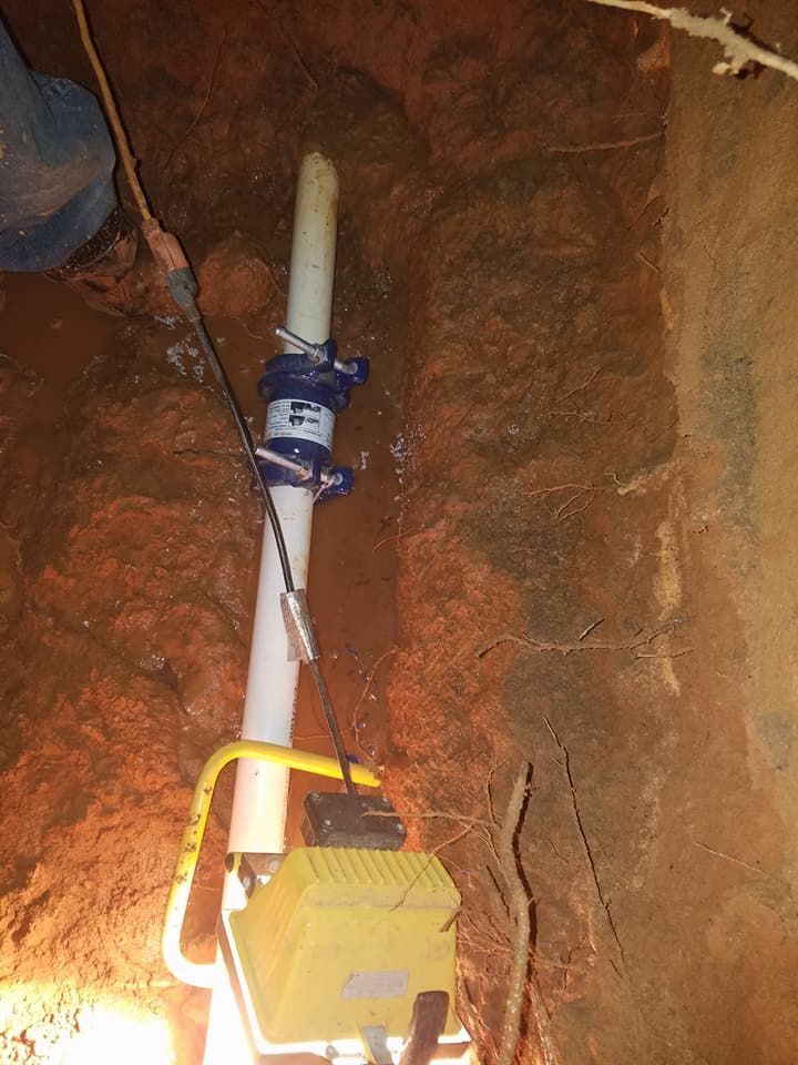 White pipe with blue clamp and yellow electrical box mounted in a dirt trench