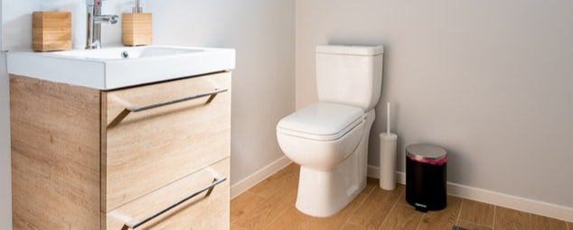 Modern bathroom with a toilet, wood vanity, and small trash can on a light wood floor