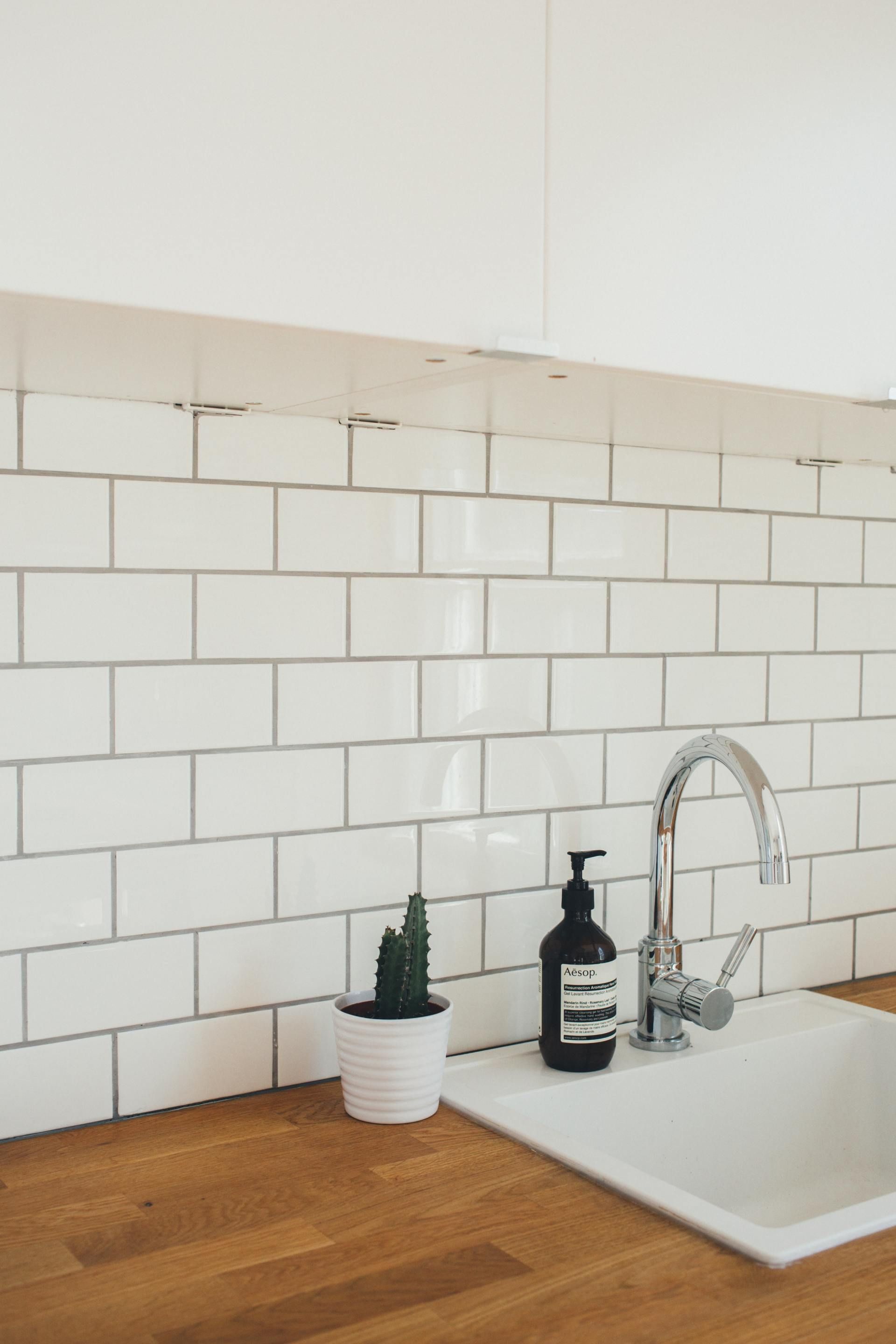 White subway-tile kitchen backsplash with wood countertop, sink, faucet, soap dispenser, and small cactus.