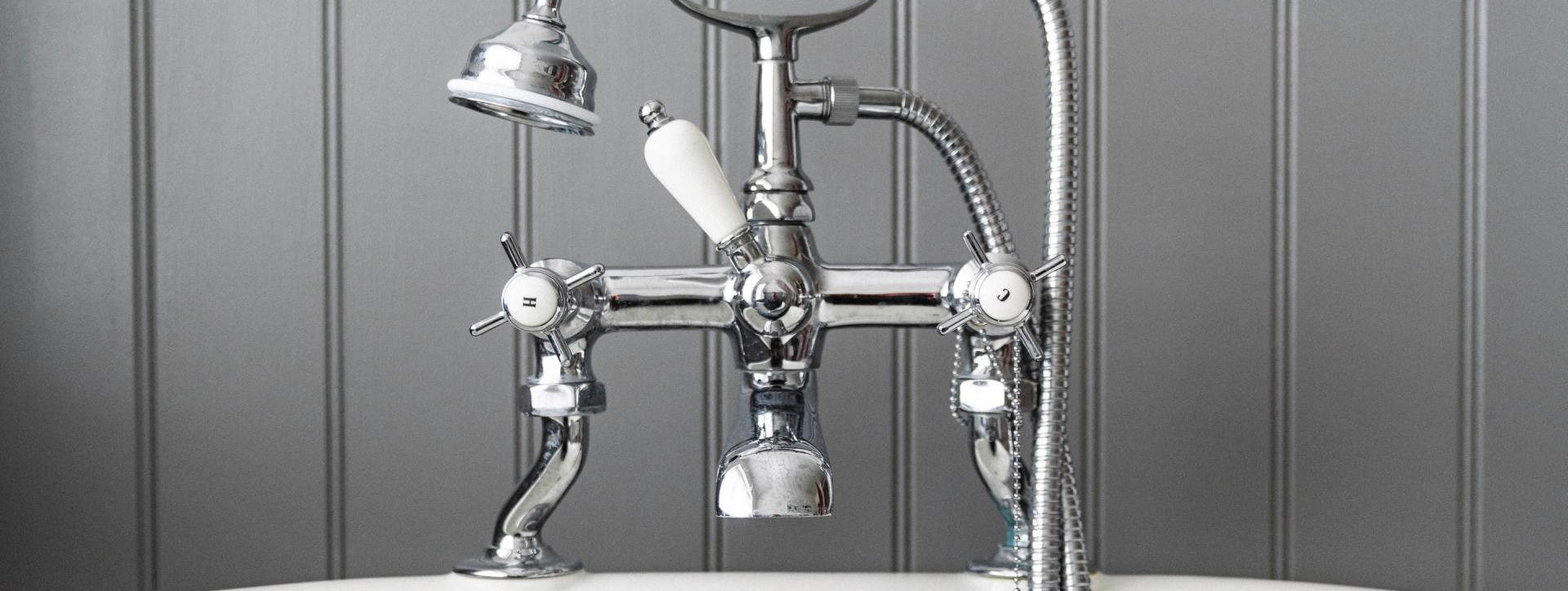 Chrome shower faucet with handheld sprayer against a gray tiled wall