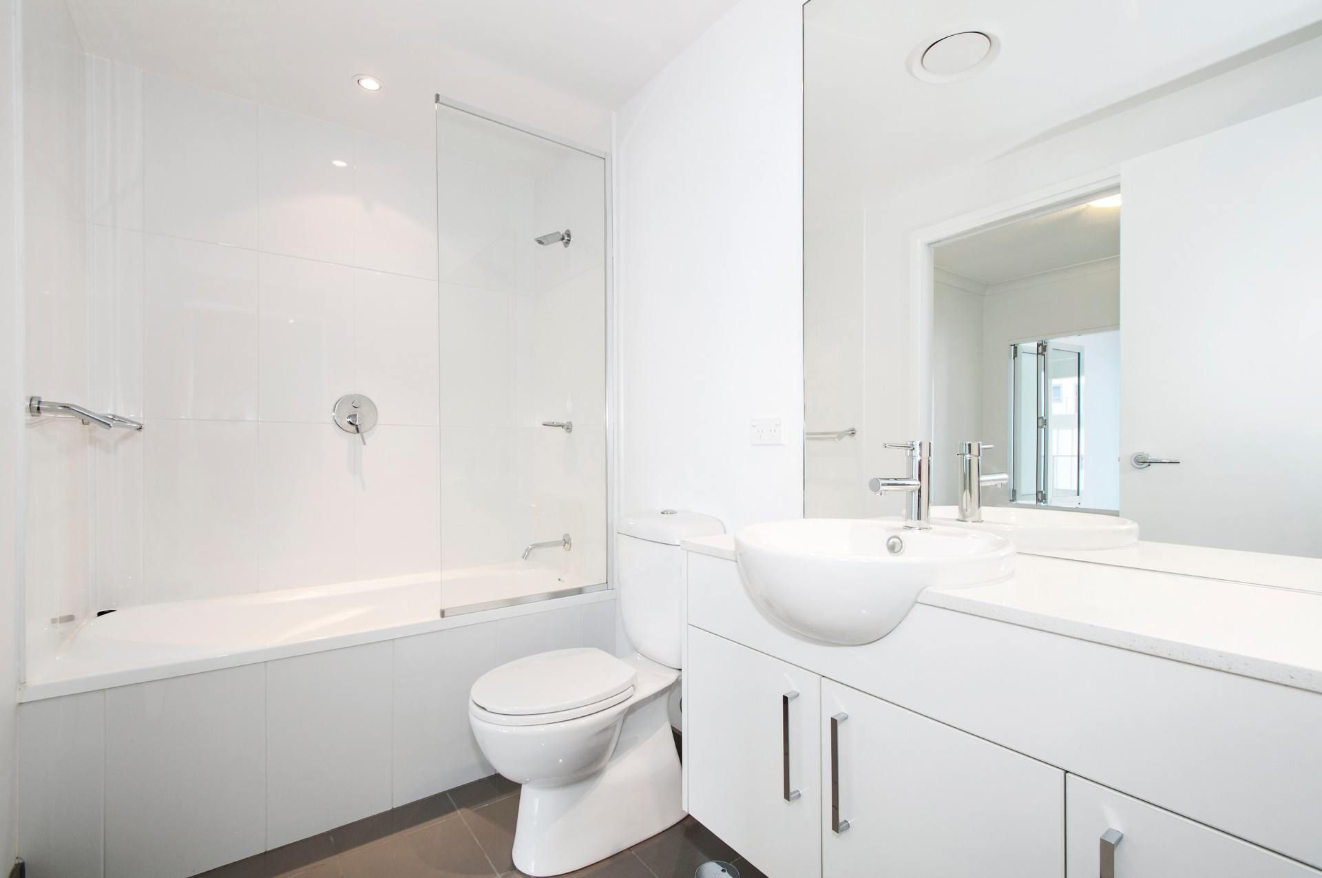 Bright modern bathroom with white tub, toilet, sink vanity, and large mirror