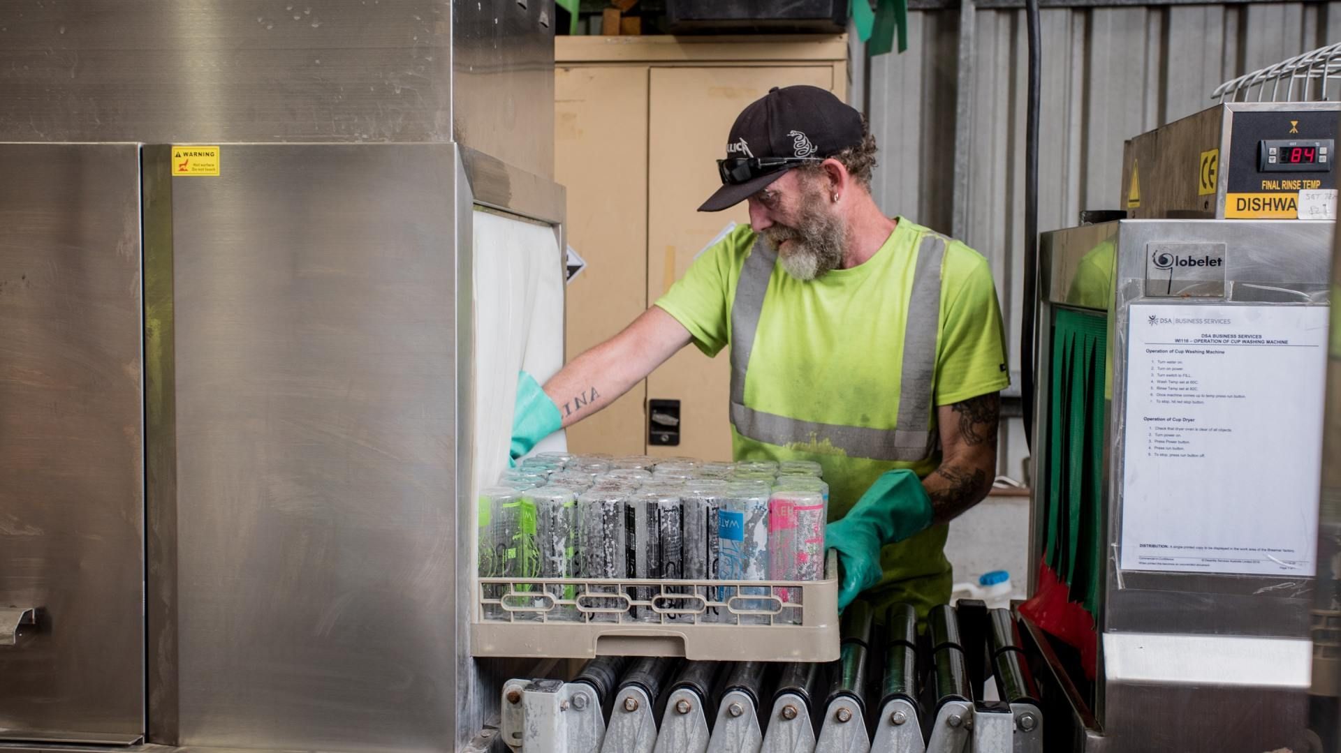 Worker in neon vest loading bottled water into a rack in an industrial kitchen or warehouse.