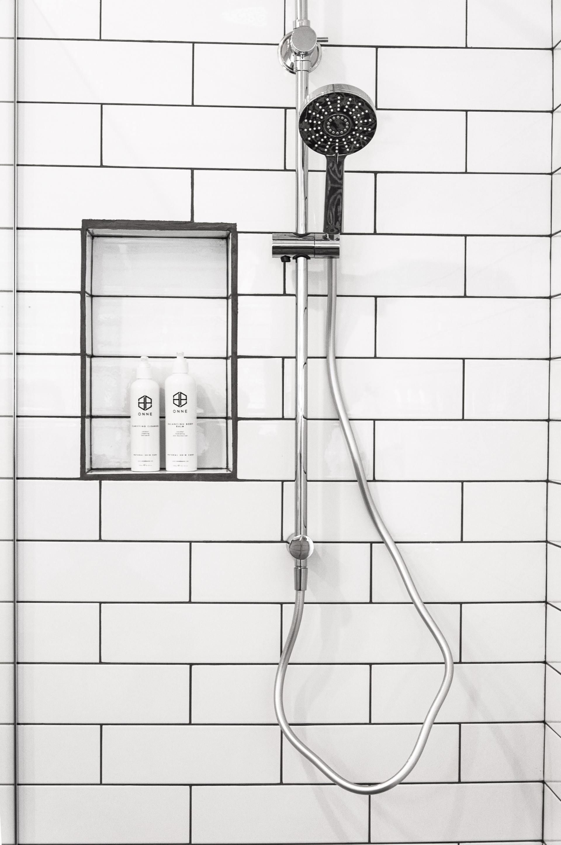 Chrome shower fixture with handheld showerhead and built-in wall shelf in white-tiled bathroom