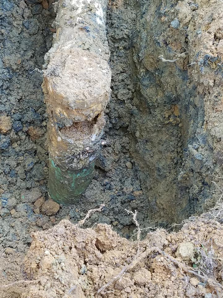 Close-up of a rusted metal pipe protruding from muddy ground and dirt-covered rock wall.