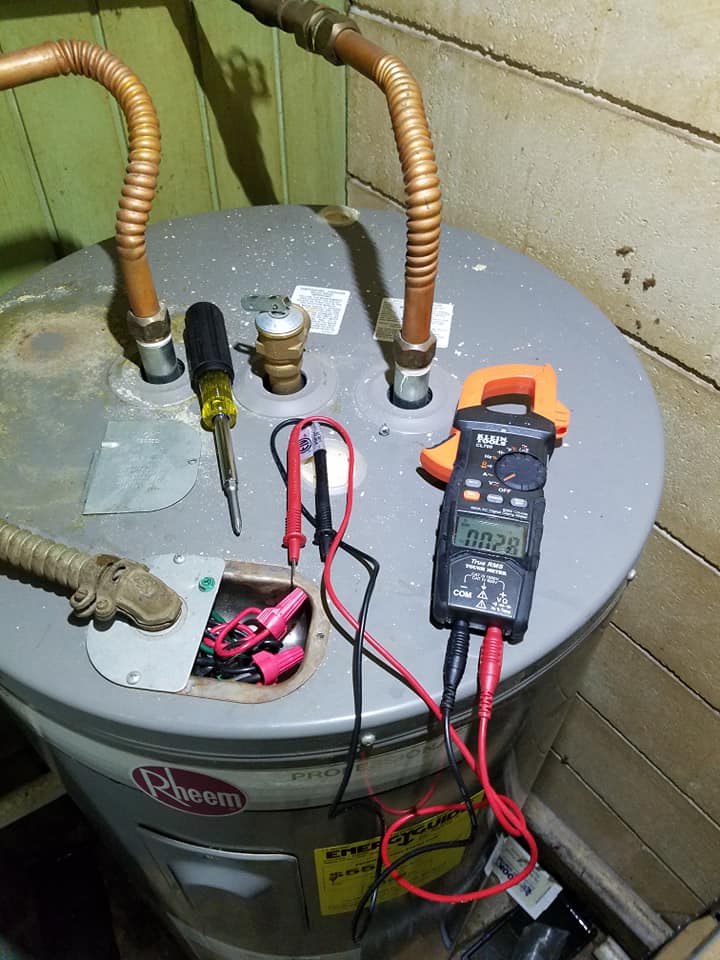 Water heater top with copper pipes, a multimeter, and red/black test leads in a utility room