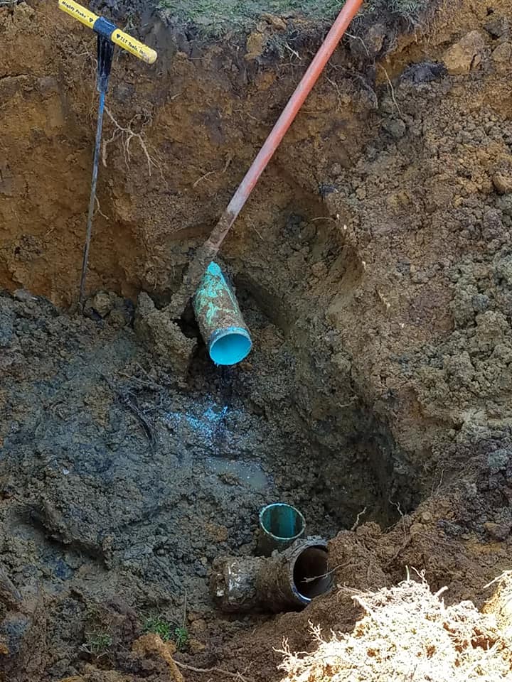 Trench with exposed underground pipes and digging tools in muddy soil