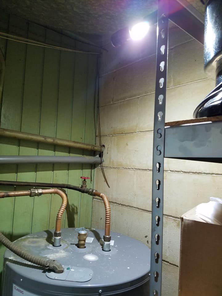 Basement utility area with water heater, copper pipes, and metal shelving under a light fixture
