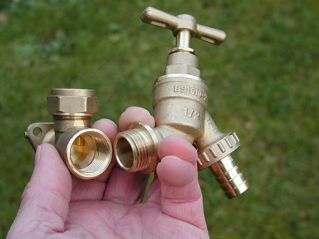 Hand holding several brass plumbing valve fittings on a light background