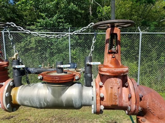 Industrial pipe valve assembly with rust-colored gate valve and silver pipe beside a chain-link fence