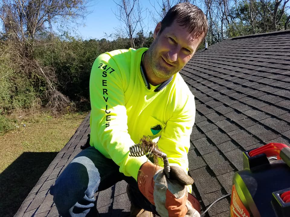 Worker in neon shirt securing a roof shingle with a tool on a sloped rooftop