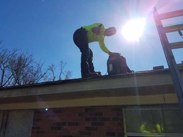 Person on a roof reaching into a bag in bright sunlight.