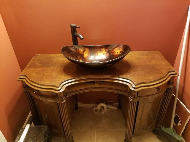 Copper vessel sink on a wooden vanity against orange walls in a small bathroom.