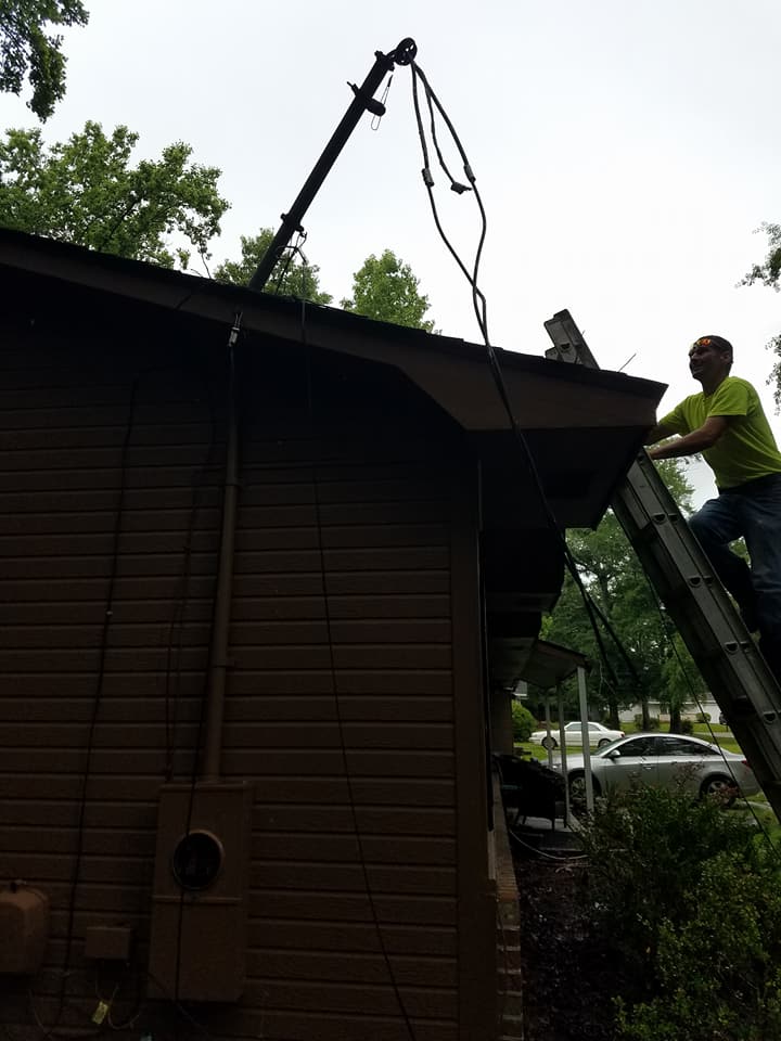 Worker on a ladder repairing a roof gutter on a dark wooden house