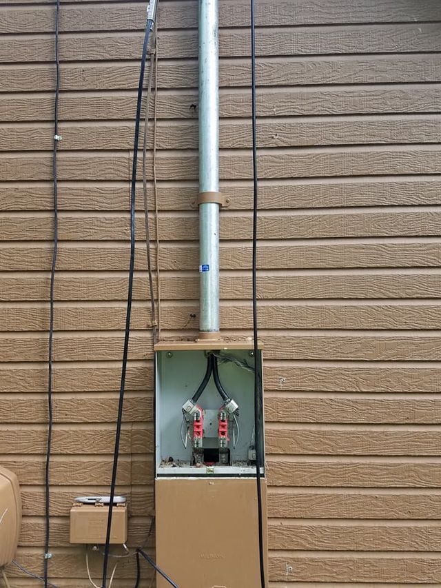 Open electrical panel with conduit pipes against a brown brick wall.