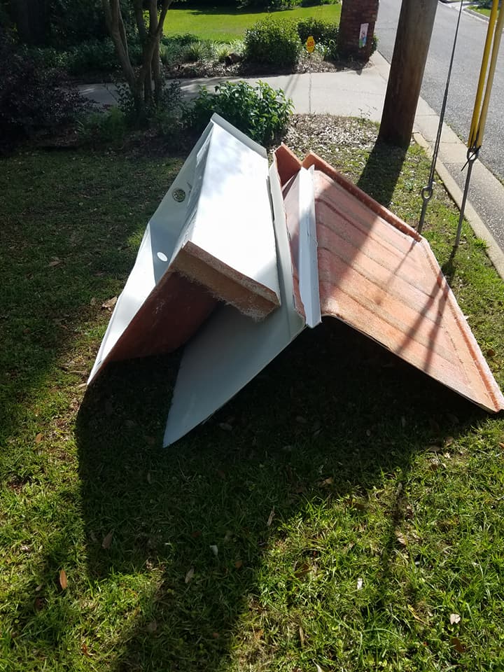 Collapsed wooden play structure on grass, with white panels and a red roof outdoors.