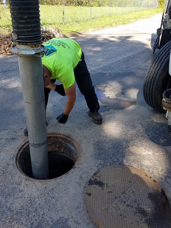 Worker in neon green shirt inspecting an open manhole beside a road.