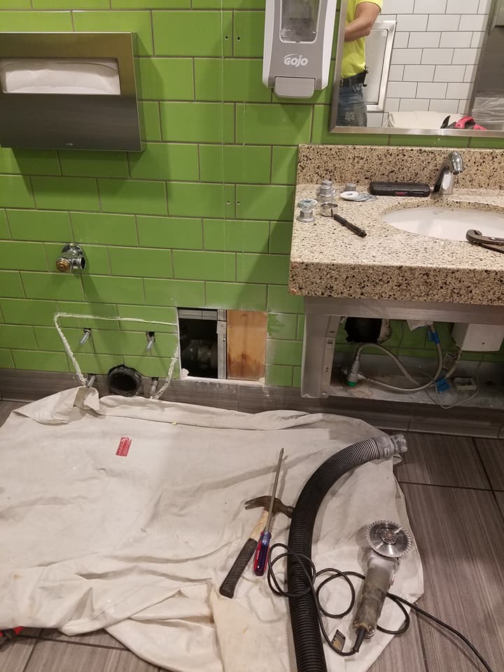 Partially demolished bathroom wall with exposed plumbing, tools, and a sink countertop being removed