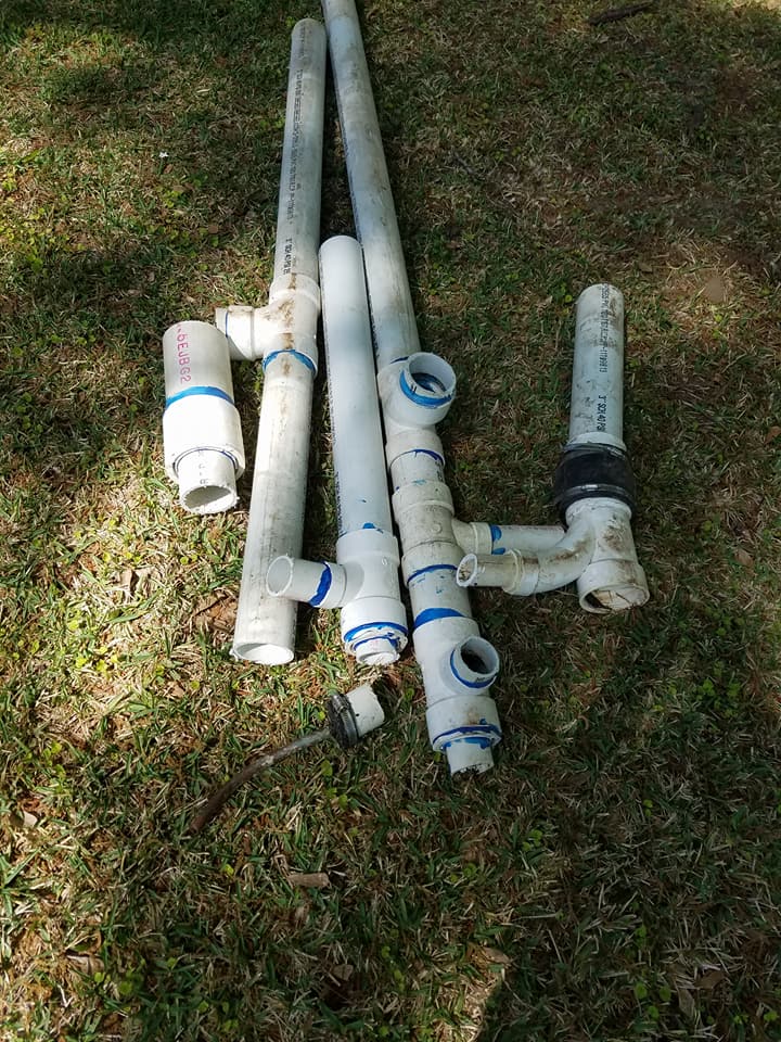 Assorted white PVC pipes and fittings laid on grass outdoors.