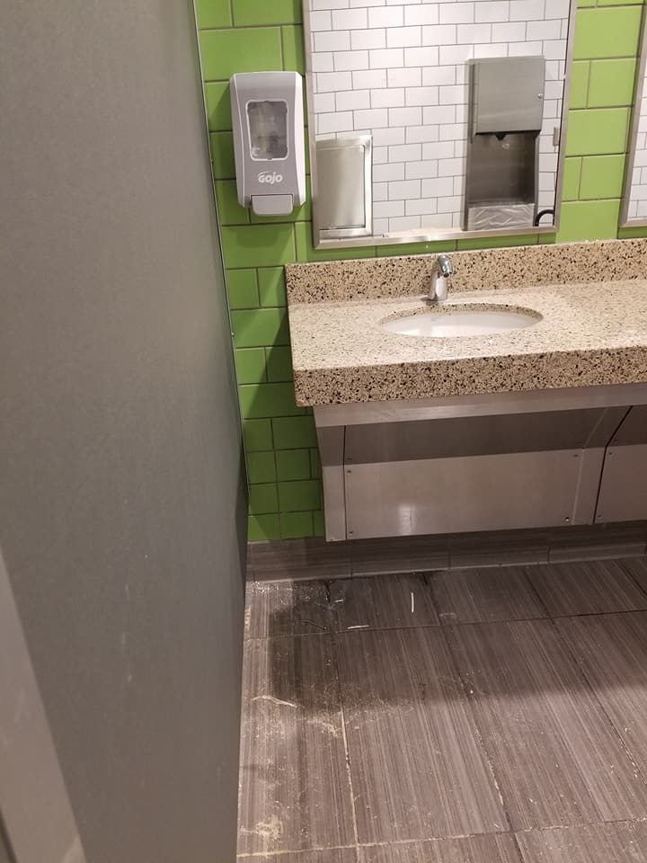 Accessible restroom sink with green wall tiles, speckled countertop, and soap dispenser next to a stall partition