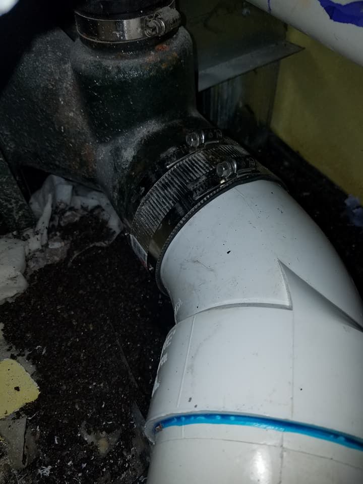 White PVC pipe connected to a dark metal fitting, with a blue ring on the elbow joint.