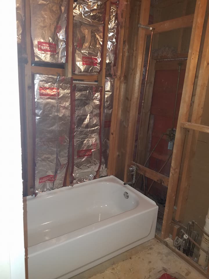 Bathroom under renovation with a white bathtub, exposed studs, and insulation behind the walls