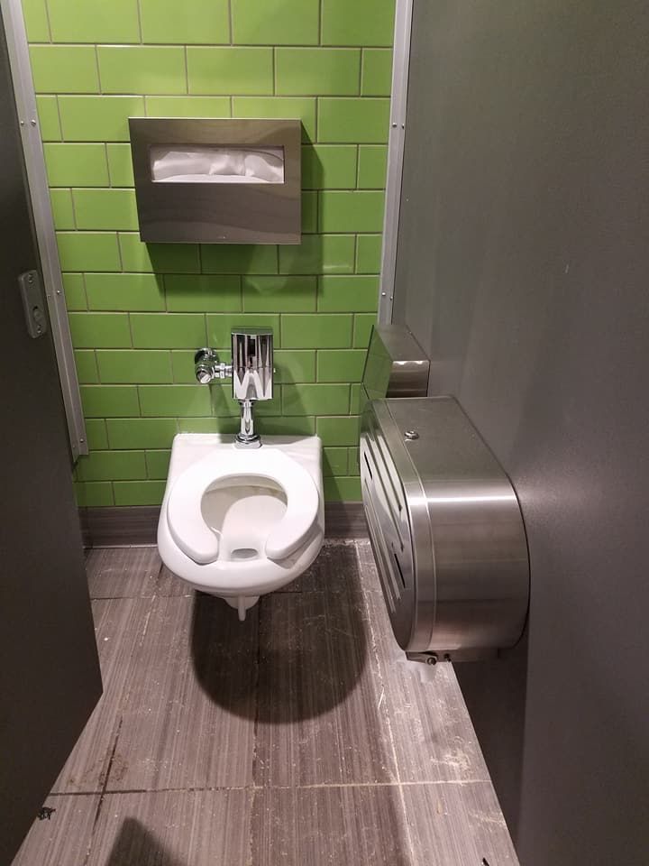 Small accessible restroom with wall-mounted toilet, green tiled wall, and stainless steel fixtures.