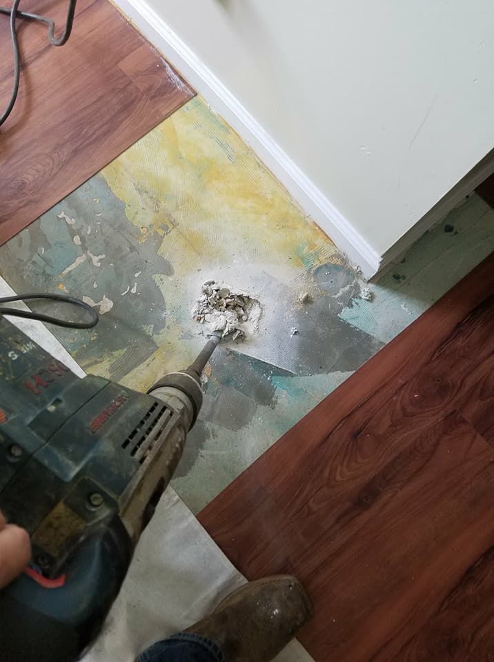 Power drill on damaged floor near wall corner, with exposed patch and debris