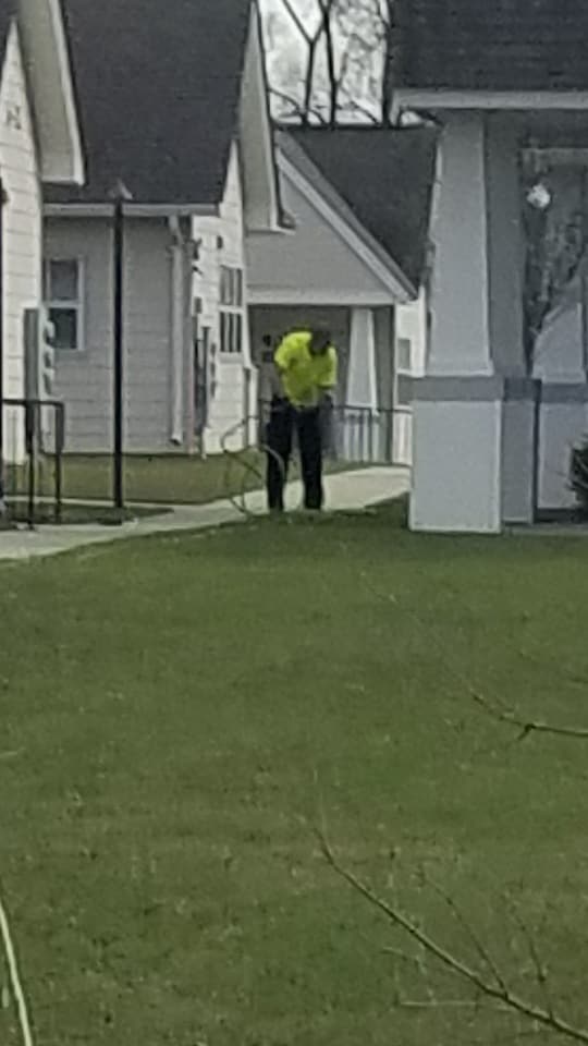 Person in a bright yellow jacket standing on a grassy lawn between houses.