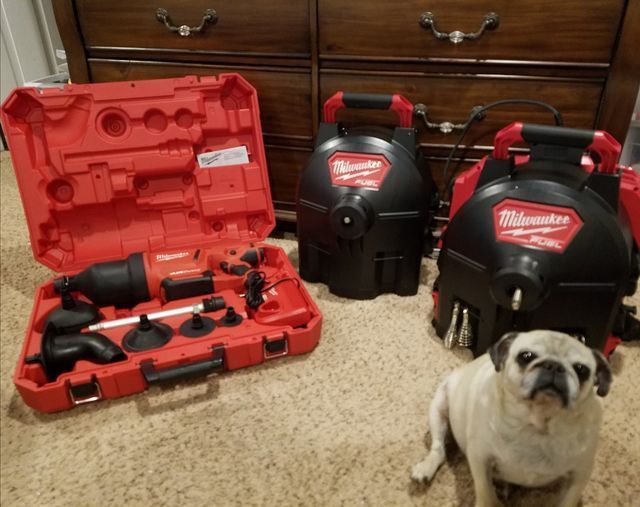 Milwaukee tools in red cases on carpet, with a small pug sitting in front of wooden drawers