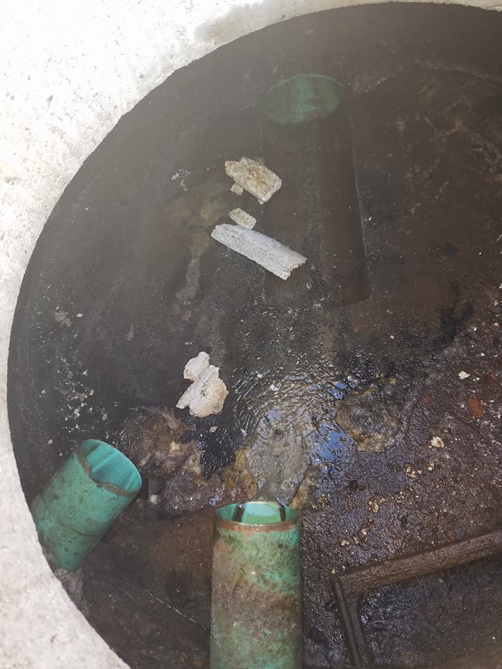 Dark circular opening with debris, white scraps, and green pipes inside a rough concrete surface