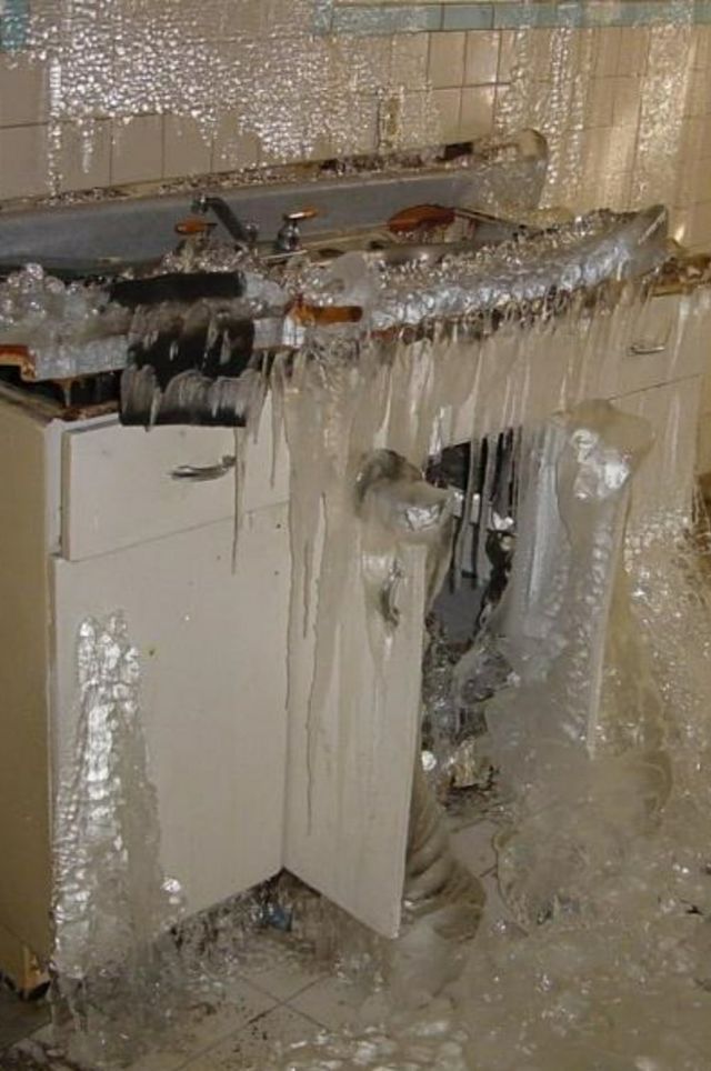 Kitchen destroyed by extensive fire damage, with melted cabinets and debris covered in plastic wrap