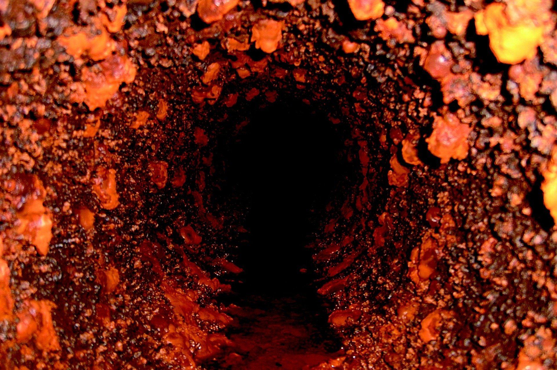 Orange coral-covered underwater tunnel opening into darkness