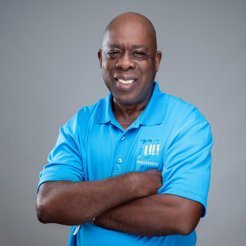A man in a blue shirt is smiling with his arms crossed.