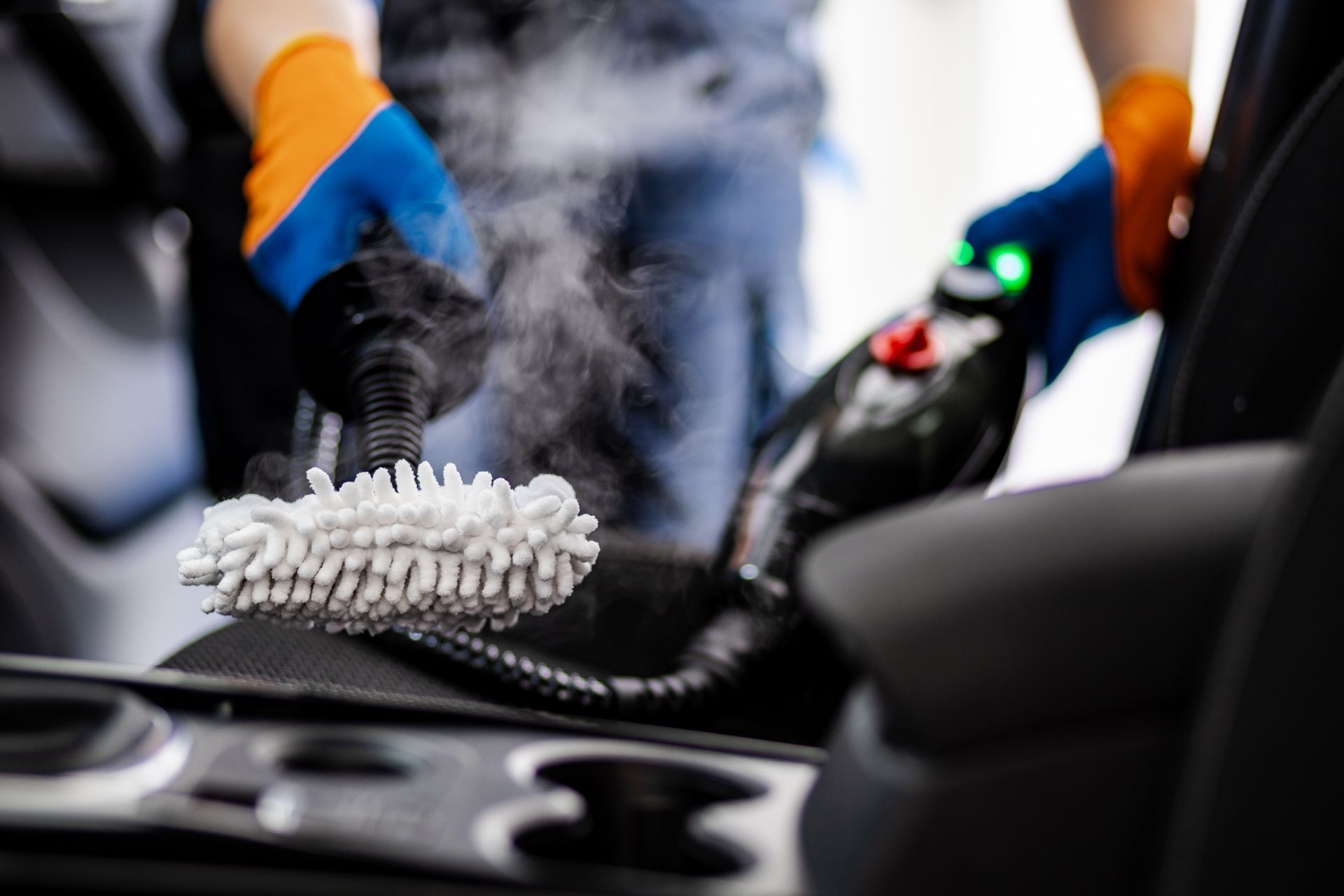 Person cleaning a car interior with a brush and spray bottle, with steam or mist visible