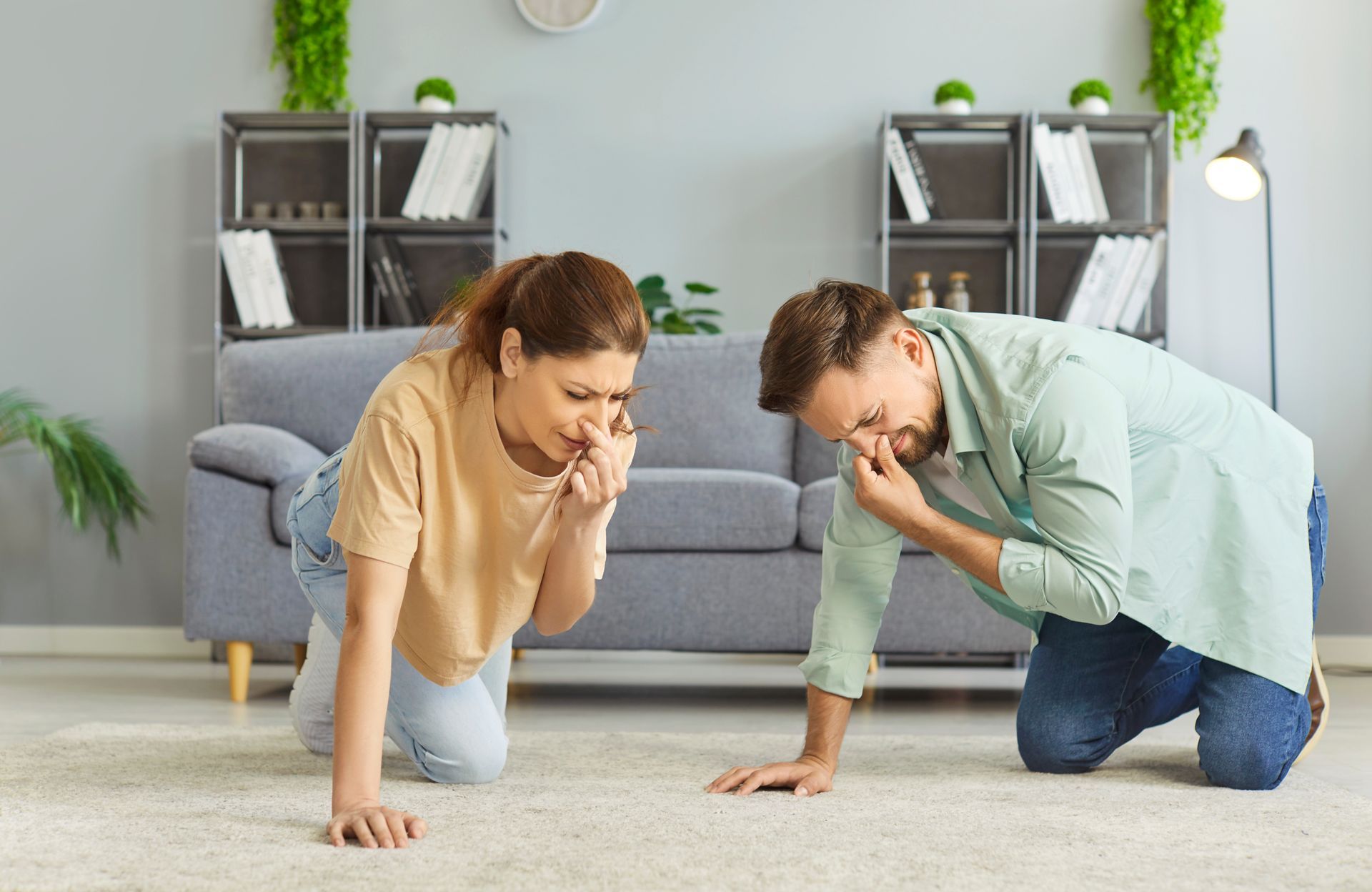 Two people kneeling on a living room floor, deep in thought, with a couch and shelves in the background.