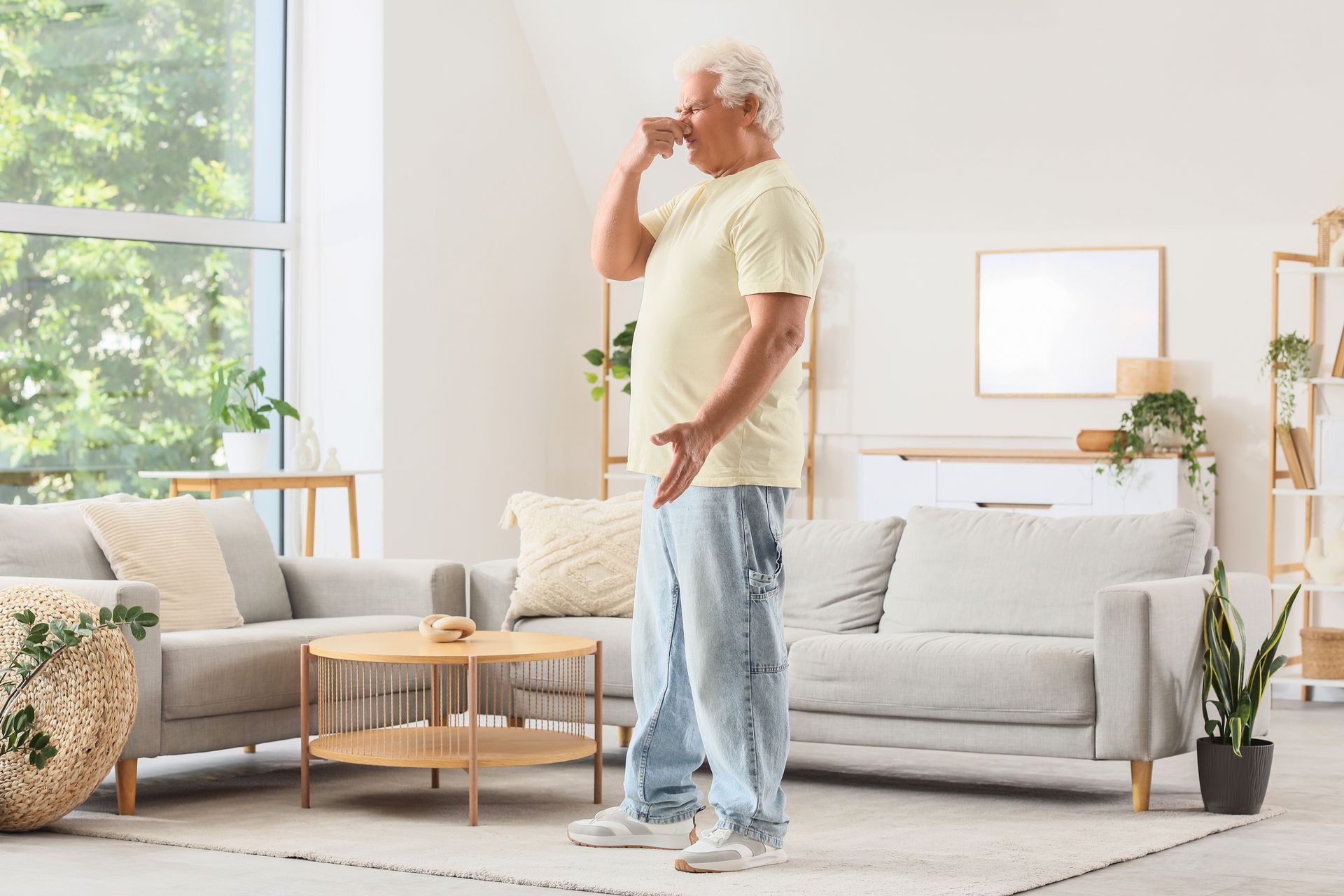 Person standing in a bright living room, drinking from a cup beside a sofa and coffee table