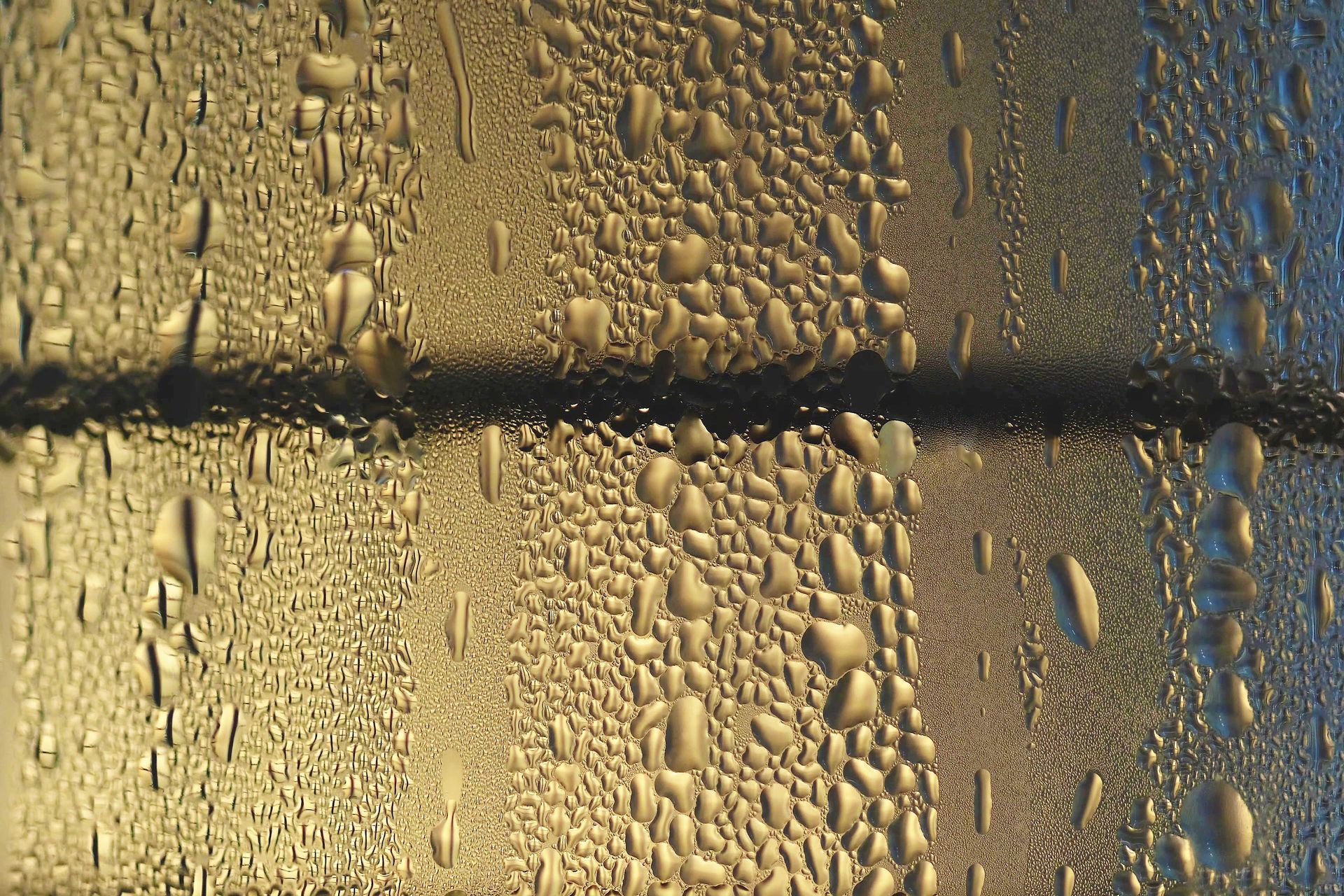 Water droplets on a glass pane, with a dark horizontal line and warm yellow-blue light behind it
