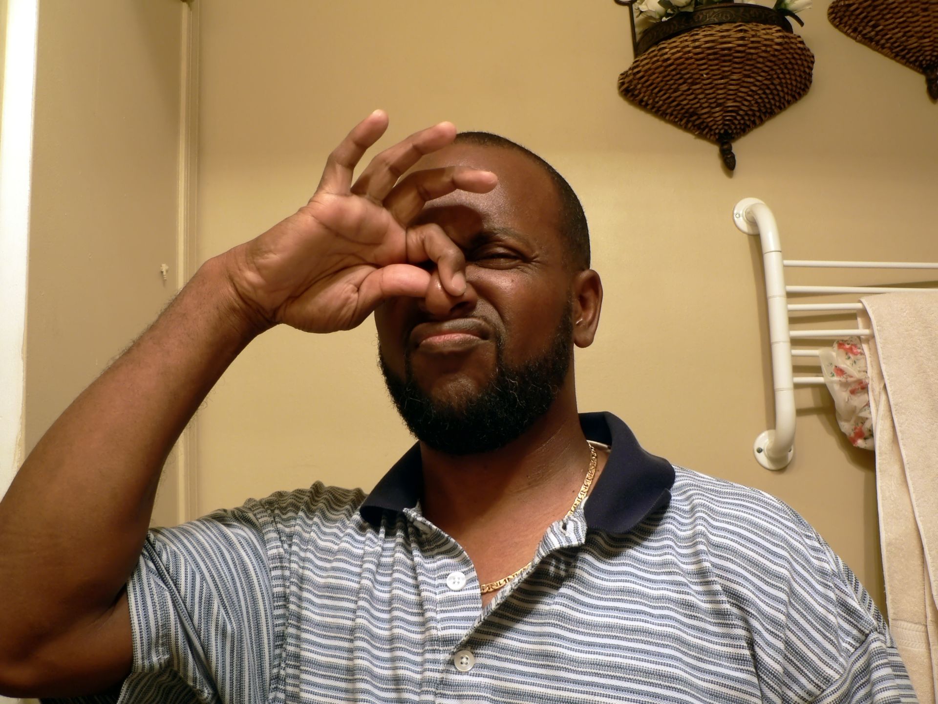 Man pinching his nose and grimacing in a bathroom, with towel rack and wicker basket in the background