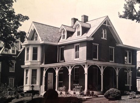 Victorian-style house with wraparound porch and gabled roof, seen from the front in sepia tones