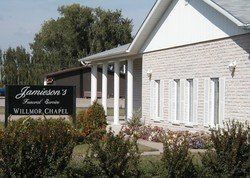 Sign for Jamison 3 at Willmor Chapel beside a white brick building and flowers