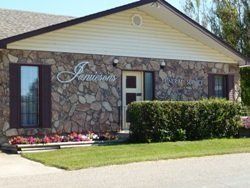 Small stone building with a light roof, window, hedge, and flower bed in front