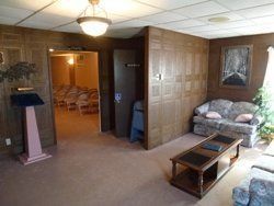 Wood-paneled lobby with chairs, coffee table, podium, and open doorway to a meeting room