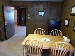 Dining nook with wooden table and chairs in a wood-paneled room, TV on the wall, and open doorway to a hallway.