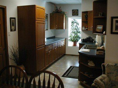 Small kitchen with wooden cabinets, tiled floor, window plants, and a table with chairs in the foreground