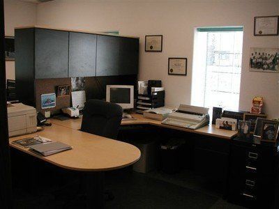 Office cubicle with dark cabinets, desk, computer monitors, printer, and window light