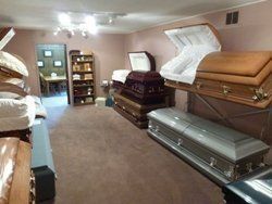 Coffin showroom with stacked caskets in a carpeted room and an open casket display in the back.